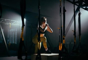 Chica en un gimnasio haciendo ejercicio físico en un banco de madera, ejercitando todas las piernas y el cuerpo