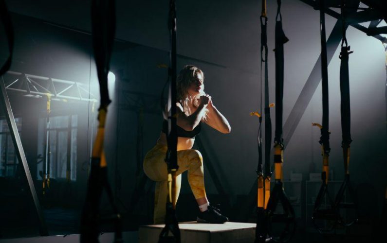 Chica en un gimnasio haciendo ejercicio físico en un banco de madera, ejercitando todas las piernas y el cuerpo